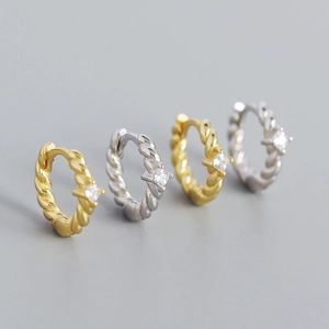 Macro shot of twisted metal hoop earrings with square zircon in gold and silver