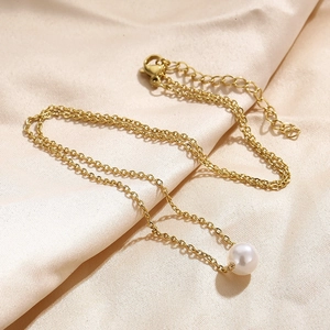 Minimalistische Goldkette mit einer einzelnen weißen Perle auf champagnerfarbener Seide