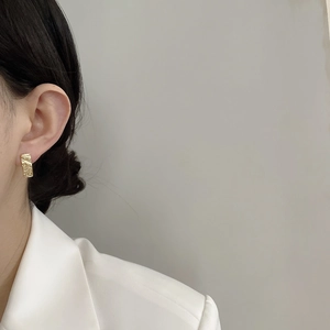 Close-up of gold rectangular stud earrings with hammered texture on a model wearing white
