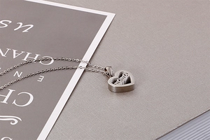 Detail of silver heart-shaped necklace with carved MAMA word on a stylish texture