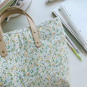 Close-up of floral tote bag featuring leather handles with brass rivets on a desk