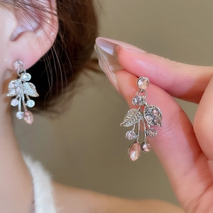Detailed view of silver leaf earrings featuring pink rhinestones held by a model