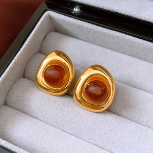 Detailed close-up of golden resin earrings with brown stones in a grey velvet jewelry box