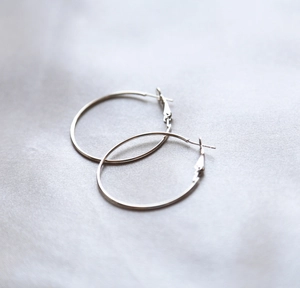 Detailed view of silver hoop earrings placed on elegant grey silk textured background