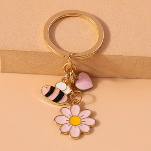 Detail showing a golden keychain with enamel bee, pink daisy, and heart charms