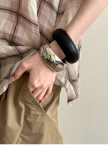 Close-up of polished silver metal bangle and matte black resin bracelet on model wrist