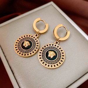 Detail of gold Medusa head earrings with Greek key pattern on red velvet fabric