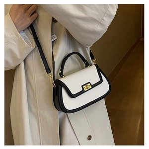 Détail d'un sac à main blanc avec bordures noires et finitions dorées porté avec un trench