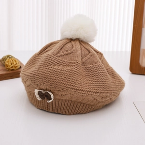 Detailed close-up of a brown cable-knit beret featuring a fur pompom and a lace bow