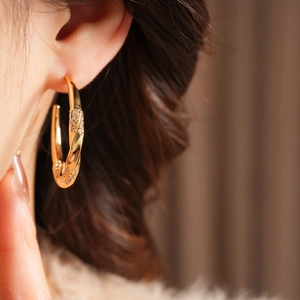 Macro side view of 18K gold plated C-shaped twisted earrings with zircon on model ear