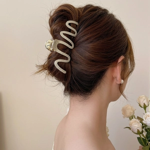 Detail of a large gold wave hair claw with sparkling rhinestones worn on a hair bun