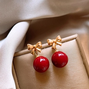 Elegant red bead earrings with gold bow detail displayed on champagne silk fabric
