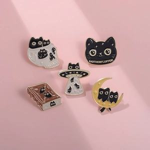 Close-up of five black cat enamel pins featuring skull, UFO, and book designs