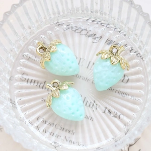 Close-up of light blue acrylic strawberry charms with golden leaf details in glassware