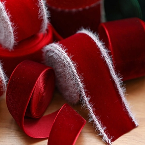 Dark red velvet Christmas ribbon with white faux feather edges stacked on wood surface
