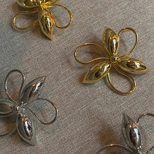 Close-up of polished gold and silver metal flower earrings on grey linen texture