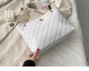 Close-up of white quilted tote bag with gold chain strap on a beige blazer setting