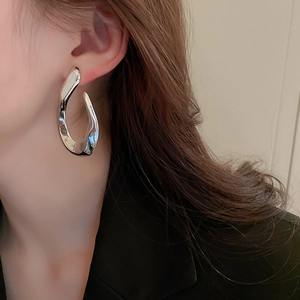 Close-up of a model wearing silver twisted geometric streamline earrings with a metallic finish