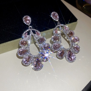 Detailed view of pink pear-shaped crystal drop earrings on light beige leather surface