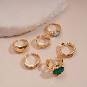 Detailed set of six vintage gold-tone rings with colorful gemstones on natural stone base