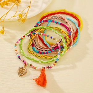 Detail of bohemian layered anklets with colorful beads, orange tassels and golden leaf pendant