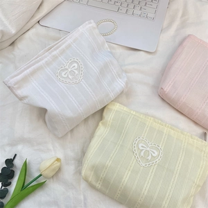 Lace bow cosmetic bags in cream, yellow, and pink on a white bed sheet setting