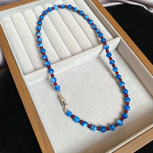 Blue and deep red beaded necklace with silver lobster clasp on a soft velvet tray