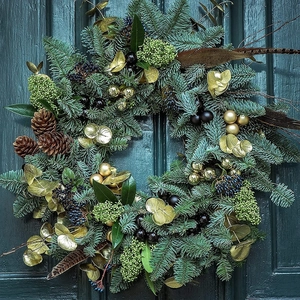 Detail of a Christmas wreath with pine cones and gold ornaments on a dark wood door