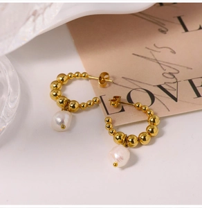 Detail of C-shaped gold beaded earrings with white baroque pearls on a vintage card