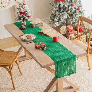Knitted green Christmas table runner with hollow design on a wooden table with decor