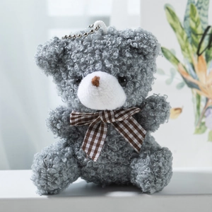 Close-up of grey plush teddy bear keychain featuring curly fur and brown plaid bowtie