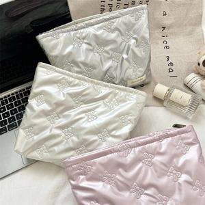 Three quilted heart pattern pouches in silver, white and pink displayed with lifestyle props
