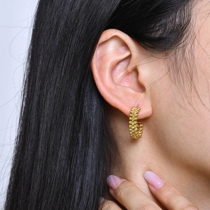 Close-up of golden stainless steel C-hoop earring with textured beads on female model