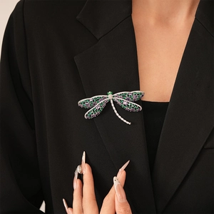Detail of a dragonfly brooch with purple and green crystals pinned on a black blazer