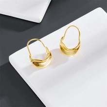 Detailed close-up of 14K gold-plated spiral hoop earrings with polished finish on white block