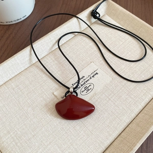 Close-up of red organic leaf-shaped pendant on black cord in a beige jewelry box