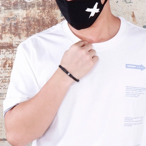 Detail of a men's black woven bracelet with a metal plate shown on a model's wrist