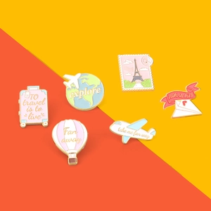 Pink travel themed enamel pins featuring airplane and globe designs on a bright background