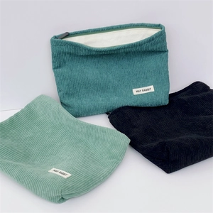 Three corduroy pouches in teal, mint, and black with zip closure and logo label detail