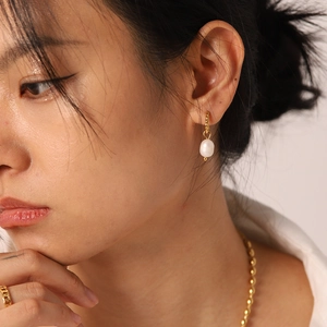 Close-up of elegant freshwater pearl drop earrings with gold twisted hoop on female model