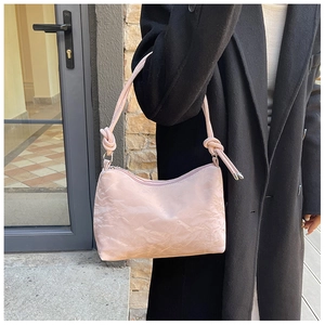 Detail of crinkled texture fabric and rope shoulder strap on a pink underarm bag