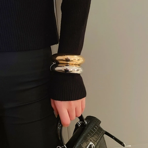 Polished chunky gold and silver bangles shown on a model's wrist against dark fabric