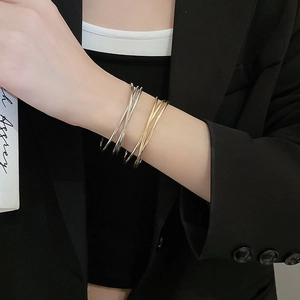 Close-up of minimalist wave cross bangles in gold and silver on a model wrist