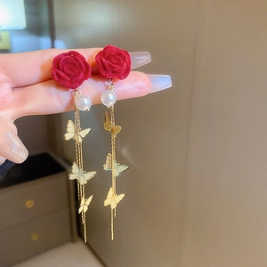 Dettaglio di orecchino lungo con rosa rossa di velluto, perla bianca e farfalla dorata