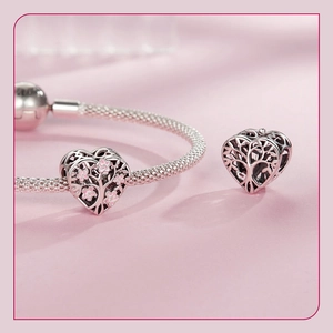 Detail of silver tree of life heart charm with pink enamel on braided bracelet