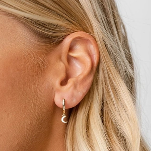 Close-up of golden crescent moon pendant earring worn on ear for women fashion
