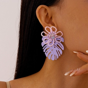 Close-up of model wearing oversized purple monstera leaf earrings with pink beaded flowers