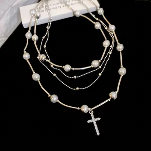 Layered pearl and metal chain necklace with a sparkling rhinestone cross pendant