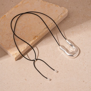 Macro shot of silver liquid metal U-shape pendant on a black cord over stone base