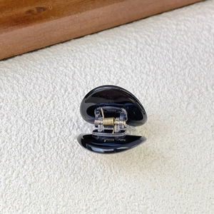 Detailed view of a small black acetate hair claw clip with a glossy finish and spring